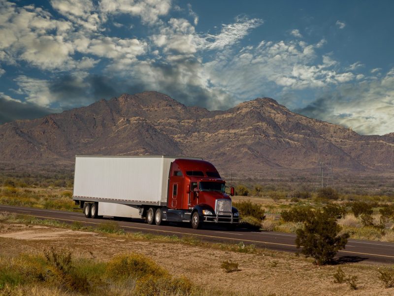 Classic big rig heavy duty long haul diesel semi truck with refrigerator semi trailer running on the road along mountains in USA